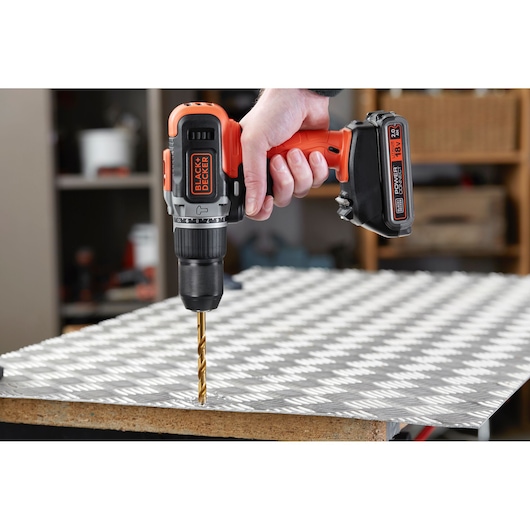 BLACK+DECKER BCD003D2AMB cordless drill in use drilling metal sheet in workshop setting.