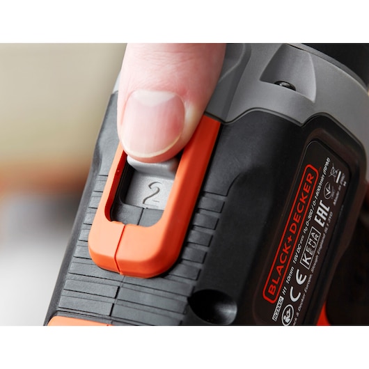 Close-up of BLACK+DECKER BCD003MEM2K drill speed switch with finger, black and orange, product photography.