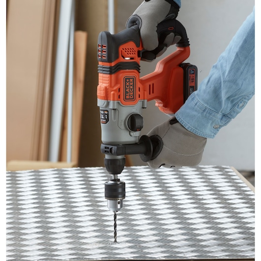 BLACK+DECKER BCD900E2K cordless hammer drill in use on a patterned metal sheet, close-up side view.