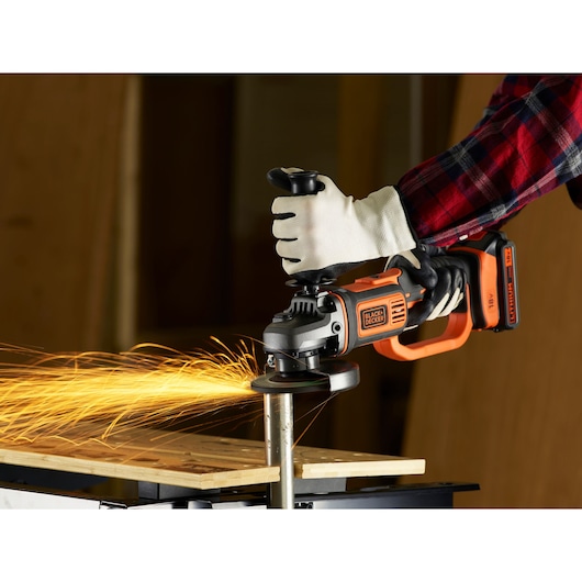 BLACKDECKER BCG720N cordless angle grinder producing sparks during metal grinding, held by gloved hand.