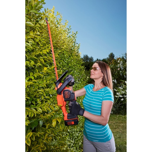 BLACKDECKER BCHTS3625L1 hedge trimmer used outdoors on green hedges, orange and black cordless tool.