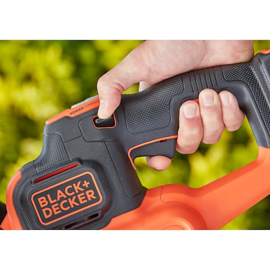 Close-up photo of BLACK+DECKER BCHTS3625L1 hedge trimmer handle with textured grip and thumb on power button.