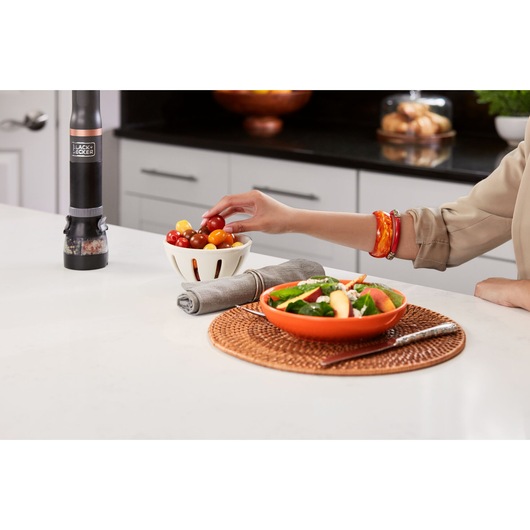 Photo of BLACK+DECKER BCKM1011KGF electric pepper grinder on a kitchen counter near a salad and tomatoes.