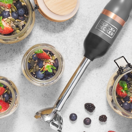 Photo of BLACK+DECKER BCKM1011KGF hand blender with metal shaft, surrounded by jars of oatmeal, berries, and seeds.