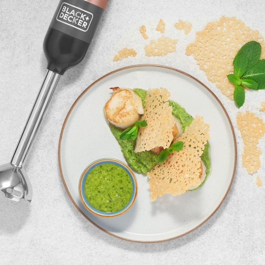 BLACK+DECKER BCKM1016KSG hand blender with metal shaft next to a plate of scallops, green sauce, and parmesan crisps.