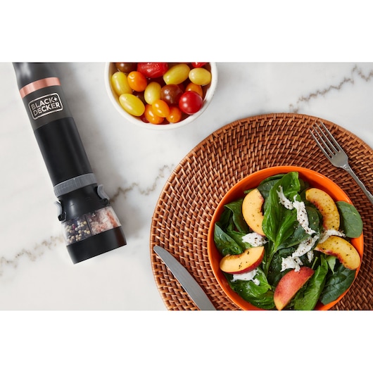 BLACK+DECKER BCKM1011KGF electric pepper mill on marble countertop near a bowl of salad and tomatoes.