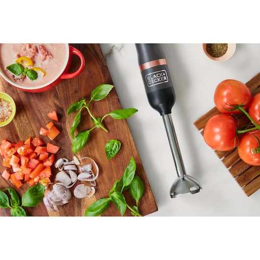 BLACK+DECKER BCKM1011KGF hand blender on a kitchen counter with fresh tomatoes, basil, and chopped vegetables.