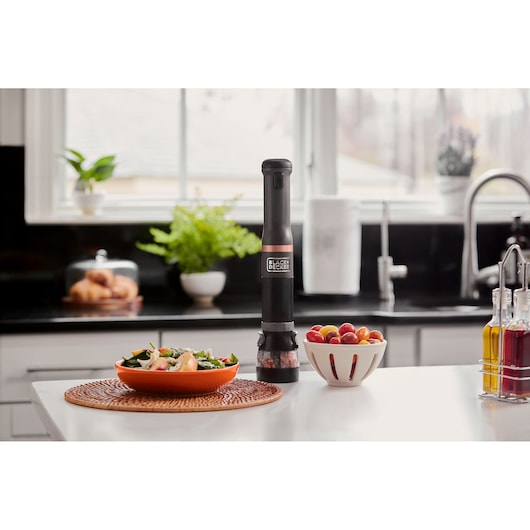 BLACK+DECKER BCKM1011KGF electric pepper grinder in black on kitchen counter, with salad and fruit bowl nearby.