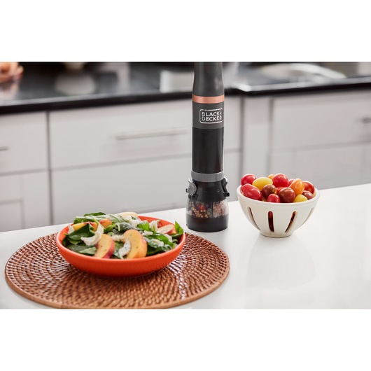 Photo of BLACK+DECKER BCKM1011KGF black electric pepper grinder on kitchen counter with salad and tomatoes.