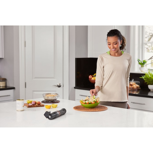 Photo of BLACKDECKER BCKM1011KGF hand mixer on kitchen counter near food and person preparing a salad.