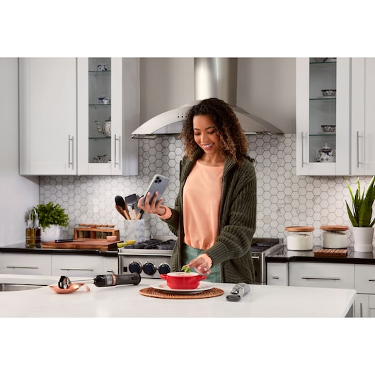 BLACKDECKER BCKM1011KGF immersion blender set with attachments on kitchen counter, person using smartphone.