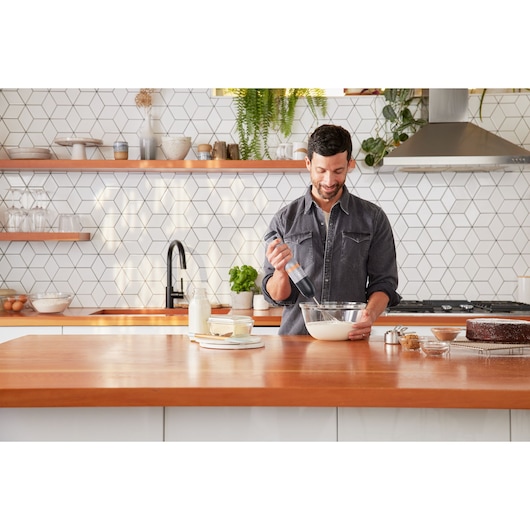 BLACKDECKER BCKM1012KG hand mixer held while mixing batter in a modern kitchen setting.
