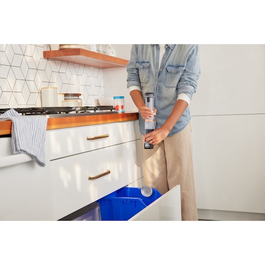 BLACKDECKER BCKM1016KSG handheld vacuum in kitchen near blue bin, held by person in denim shirt.