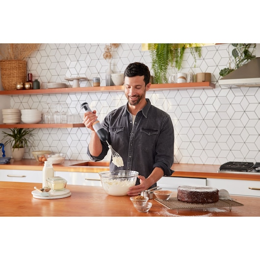 BLACKDECKER BCKM1016KSG hand mixer used in kitchen to mix ingredients in glass bowl next to cake and milk.