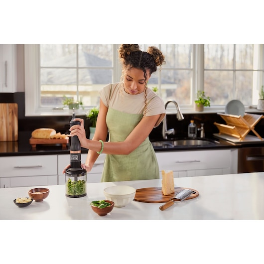 Photo of BLACKDECKER BCKM101FP immersion blender in use, blending greens in a kitchen setting.