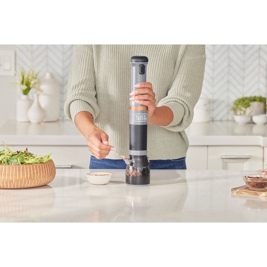 BLACKDECKER electric pepper grinder BCKM101SPFF in use on a kitchen countertop, person dispensing spice.