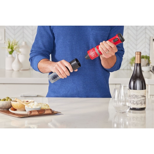 Photo of person using BLACK+DECKER BCKM101WNFF electric wine opener in a modern kitchen near a wine bottle and glasses.
