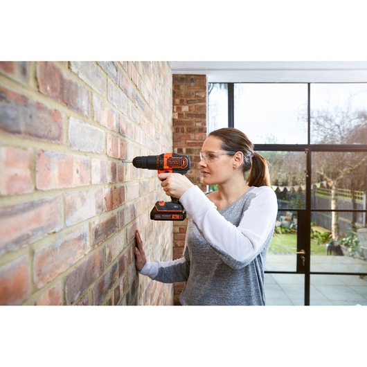 Person using BLACKDECKER BCKSB05 cordless drill on brick wall indoors, photo shows side profile with drill in action.