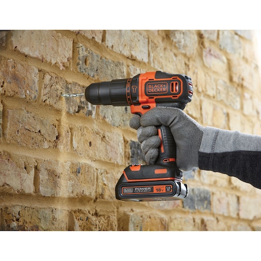 BLACKDECKER BCKSB05 cordless drill in use drilling into brick wall, close-up side view with glove-covered hand.