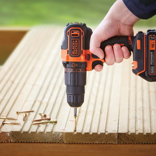 BLACK+DECKER BCKSB05 cordless drill driving a screw into wooden planks, hand holding the tool, close-up.