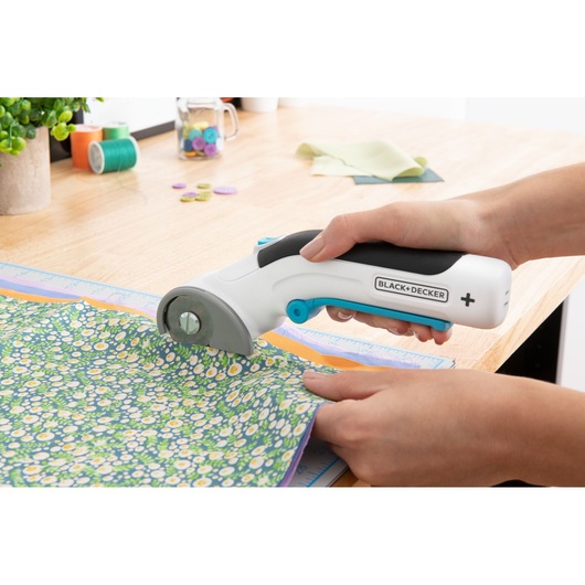 BLACK+DECKER BCRC115 rotary fabric cutter in use on floral fabric, handheld on workspace.