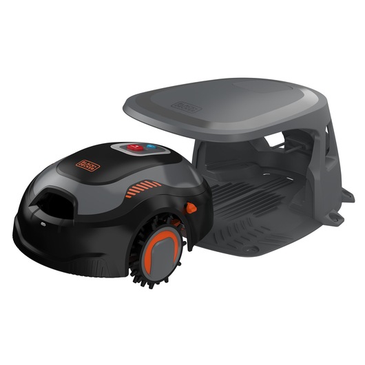 A BLACK+DECKER robotic lawn mower, model BCRMW123, shown next to its protective charging station. The mower is black with orange accents and has control buttons on top.