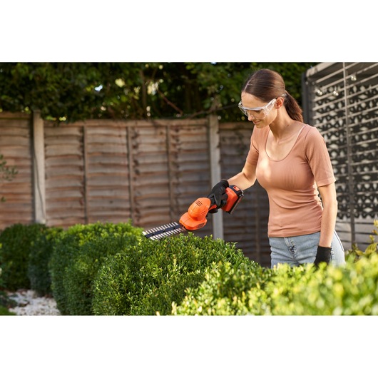 BLACKDECKER BCSS18B hedge trimmer in use outdoors trimming green bushes.