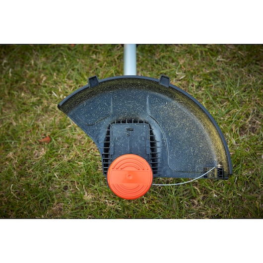 BLACKDECKER BCSTE636L1 grass trimmer head with black debris guard and orange spool, close-up on grass.