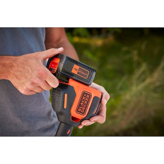Photo of BLACKDECKER BCSTE636L1 36V lithium battery being inserted into orange and black power tool outdoors.