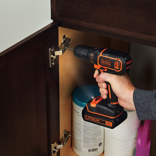 BLACKDECKER BDCDC18K cordless drill used on cabinet hinge, orange and black design, 18V lithium battery.