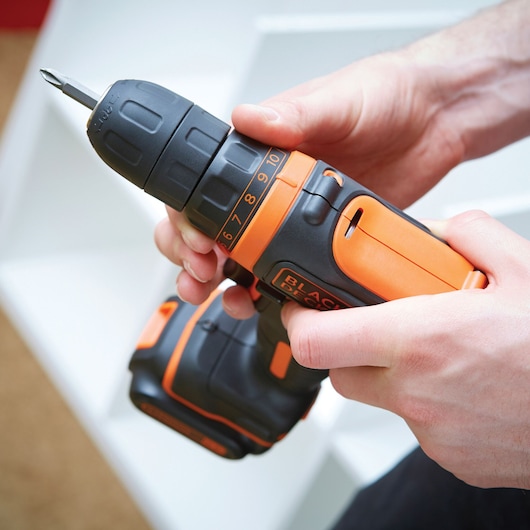 Photo of BLACK+DECKER BDCDD121 cordless drill with orange and black casing, shown in use by hands.