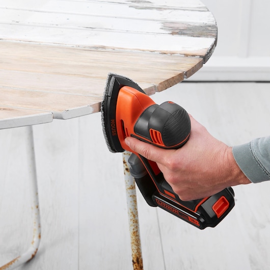 BLACKDECKER BDCDS18 cordless mouse sander sanding edge of round wooden table, side angle.