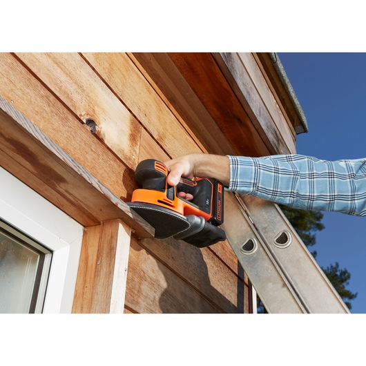 BLACKDECKER BDCDS18 cordless sander used on wooden exterior siding, close-up action scene.