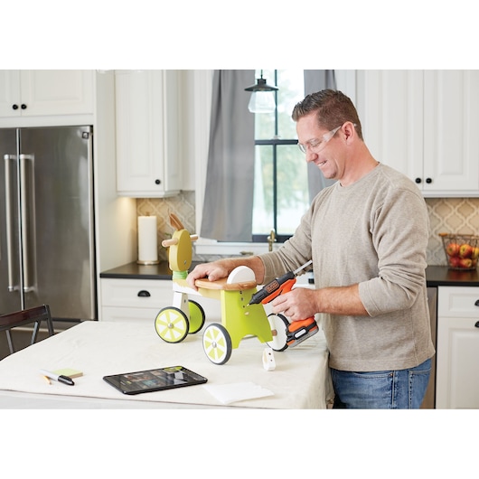 Photo of BLACKDECKER BDCGG12N cordless glue gun used to assemble a wooden toy bike in a kitchen setting.