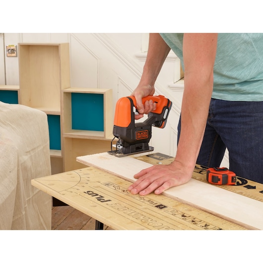 BLACK+DECKER BDCJS12N jigsaw in use cutting wood, shown in a workshop setting.
