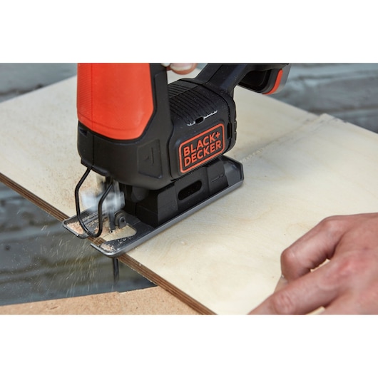 Photo of BLACK+DECKER BDCJS12N jigsaw cutting plywood, close-up on tool and user's hand.