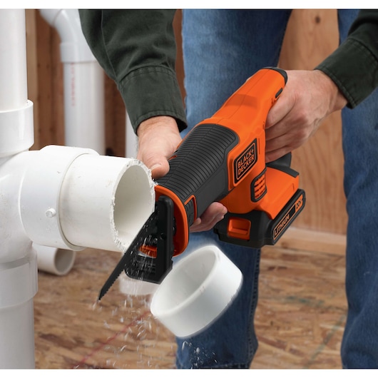 BLACKDECKER BDCR18 cordless reciprocating saw cutting white plastic pipe, close-up angle.