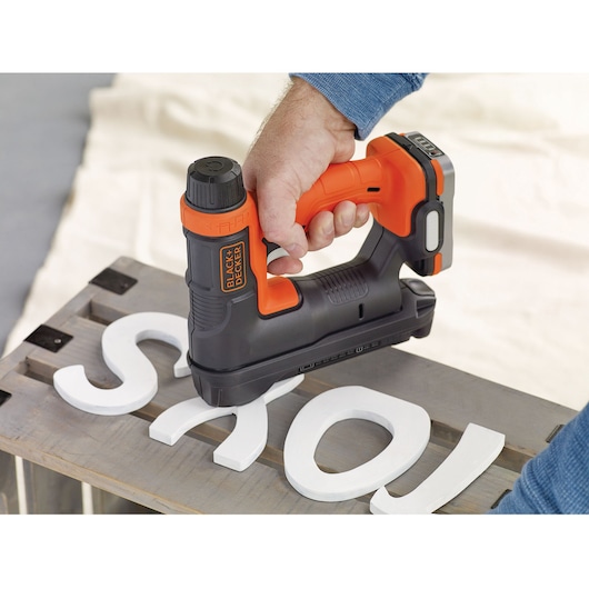 BLACK+DECKER BDCT12N cordless nail gun in use attaching white wooden letters to a wooden surface.