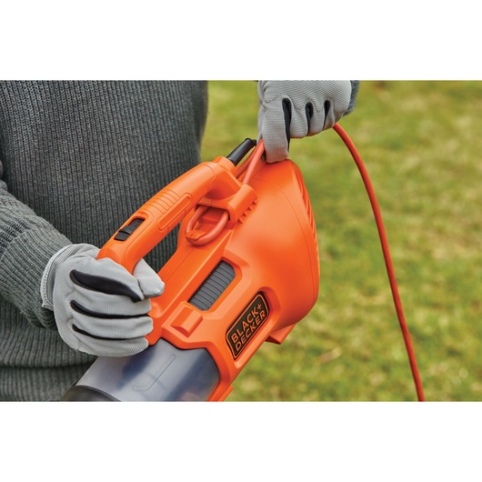 Photo of BLACKDECKER BEBL185 orange handheld leaf blower with cord held by gloved hands outdoors.