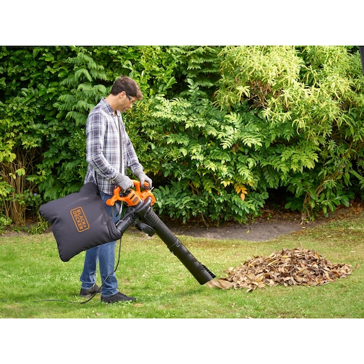 BLACKDECKER BEBLV260 leaf blower with collection bag in use outdoors near pile of dry leaves.