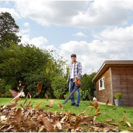 BLACKDECKER BEBLV290 leaf blower in use outdoors blowing leaves near wooden shed.