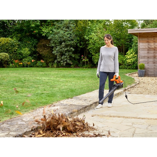 BLACKDECKER BEBLV290 leaf blower being used in a garden setting on stone pavement.