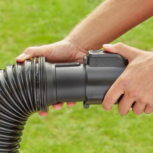 Close-up photo of hands attaching BLACK+DECKER BEBLV290 black vacuum hose outdoors.