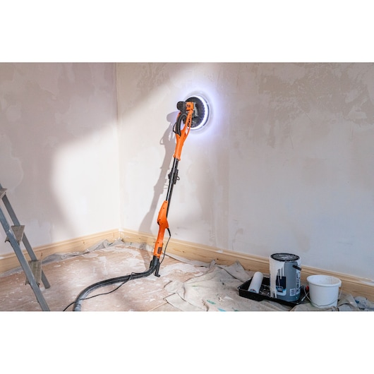 BLACK+DECKER wall sander with LED light used for smoothing plaster in a room corner during renovation.