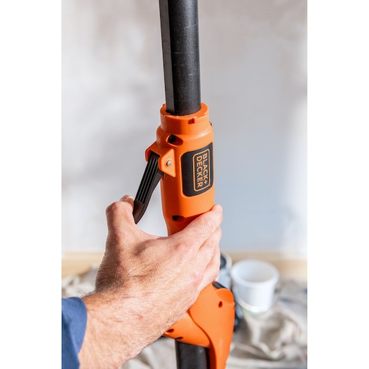 Hand adjusts orange BLACK+DECKER BEDW700 tool handle, indoor setting with blurry background.