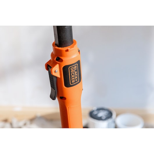 Close-up of an orange BLACK+DECKER tool handle with a black trigger, shown indoors against a blurred background.