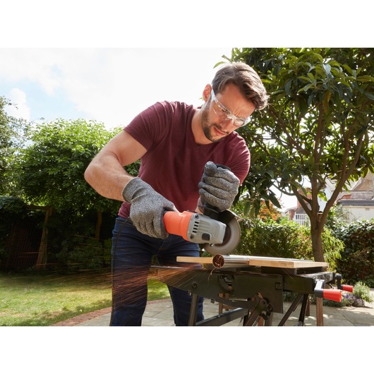 Photo of BLACKDECKER BEG010 angle grinder cutting metal outdoors, sparks flying, operator wearing gloves.