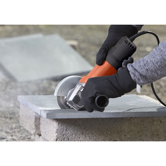 BLACKDECKER BEG110 angle grinder in use cutting a stone slab, close up of hands wearing gloves.