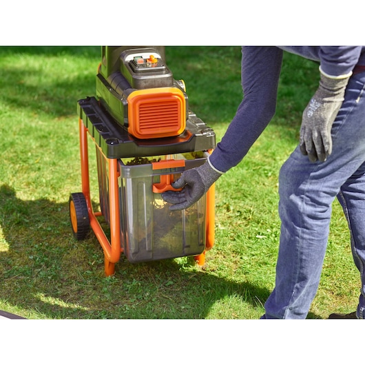 Photo of BLACKDECKER BEGAS5800 garden shredder with clear collection box, person wearing gloves on handle outdoors.