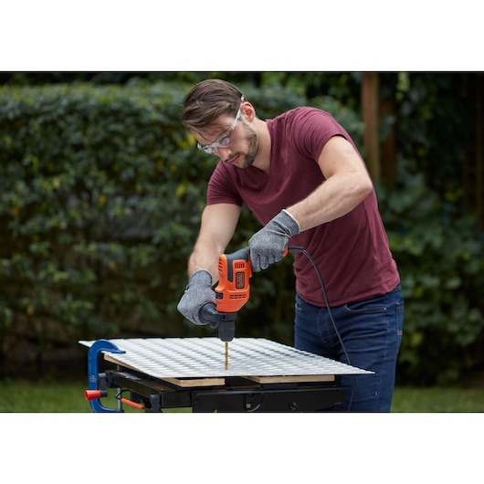 Photo of a person using a BLACKDECKER BEH200 corded drill on a workbench outdoors, drilling into a metal sheet.